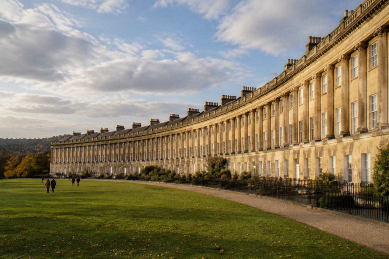 Curved Georgian terraced houses in honey-coloured stone above a green lawn, Bath, late afternoon
