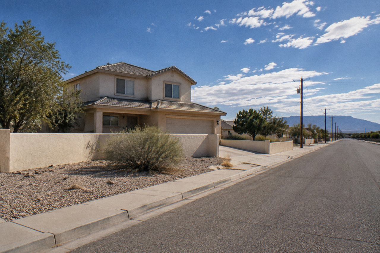 Suburban stucco house behind low wall under bright New Mexico sky