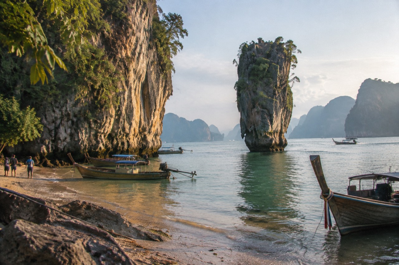 Slender limestone sea stack beside a leaning karst cliff on a Thai bay beach