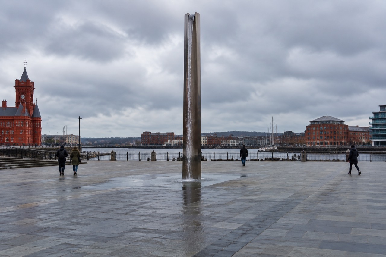 Tall steel pillar on a paved plaza by Cardiff Bay waterfront under grey clouds
