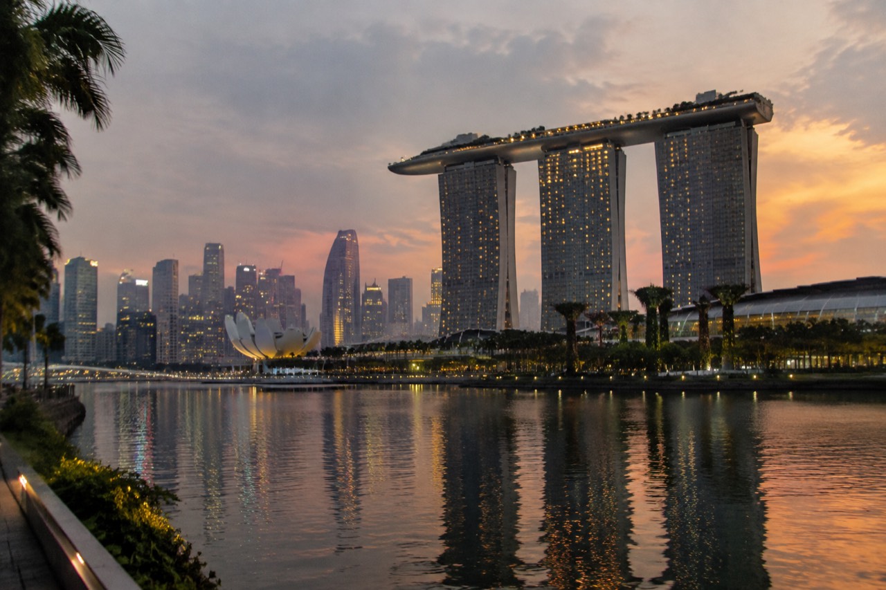 Three glass towers topped by a curved sky park glowing at dusk over the bay.