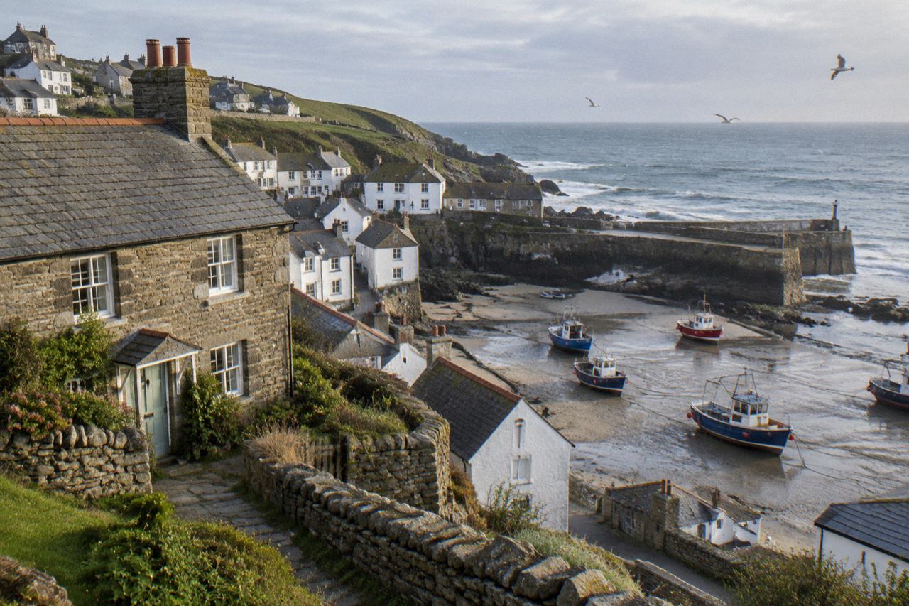 Stone cottage above a small Cornish harbour with boats on wet sand
