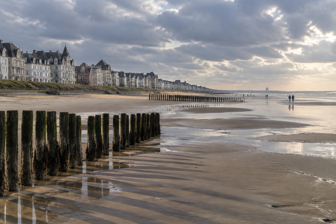 Wide sandy beach at low tide with wooden groynes under grey skies at Dunkerque.