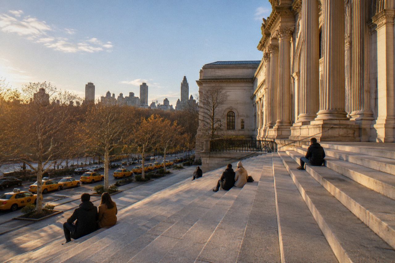 Wide limestone museum steps on Fifth Avenue with seated figures, taxis and bare trees.