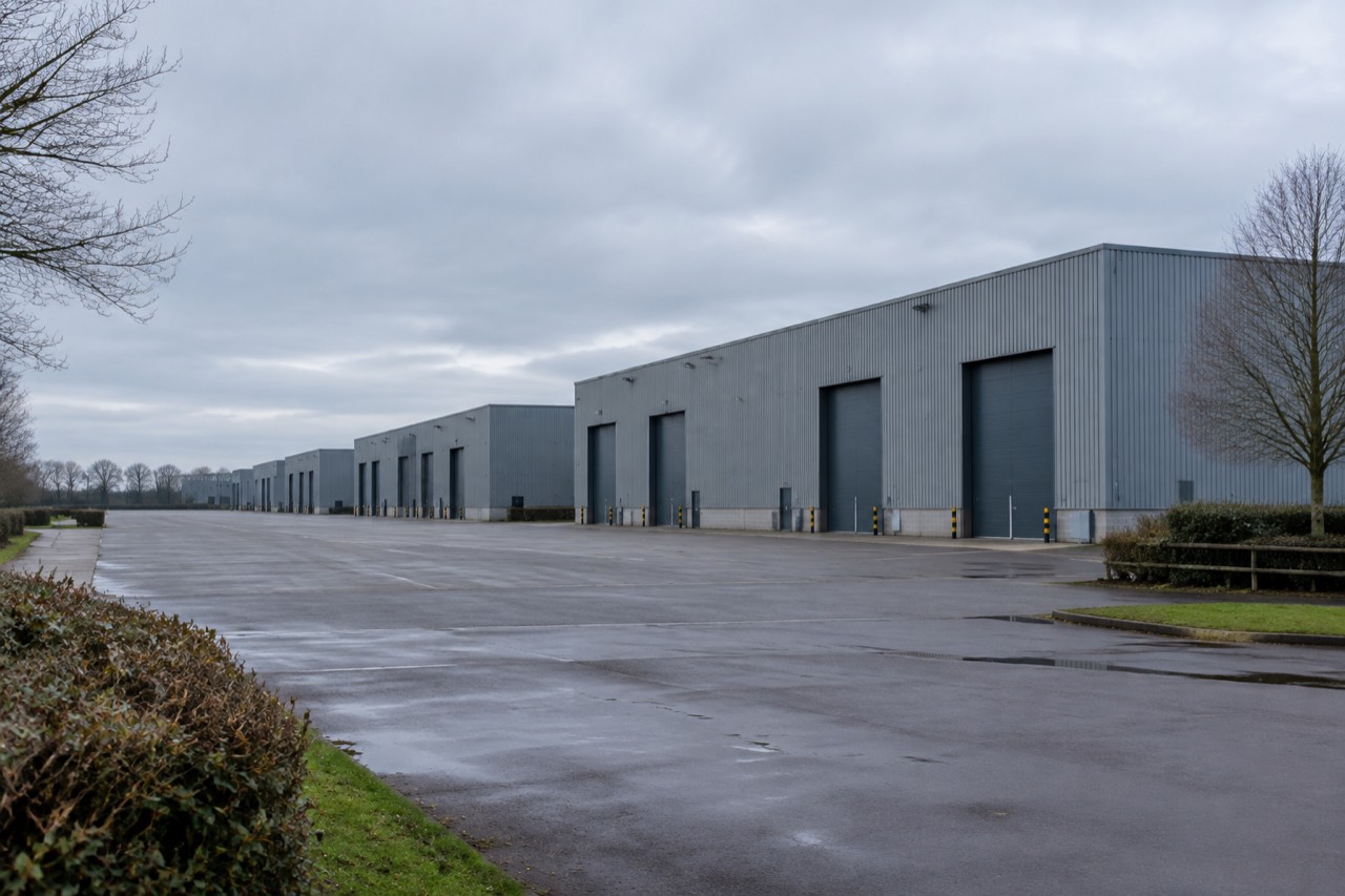 Grey studio sound stages beside an empty forecourt under overcast skies, hedgerows and bare winter trees.