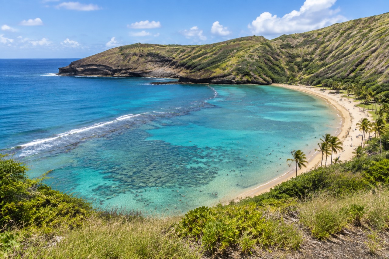 Curved turquoise bay seen from a crater rim overlook, green slopes and sandy beach
