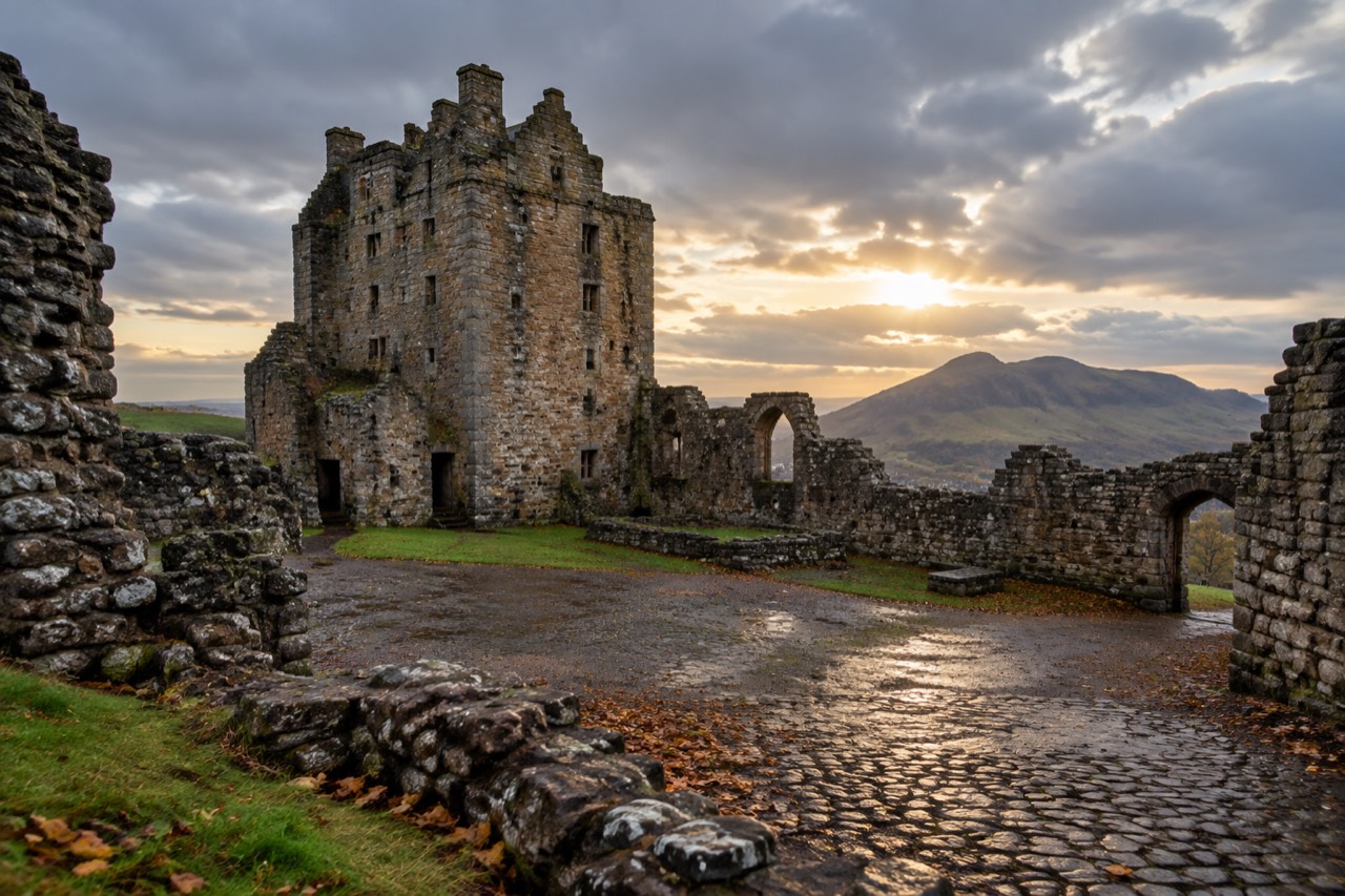 Ruined stone castle tower and walls on a grassy hill beneath cloudy skies