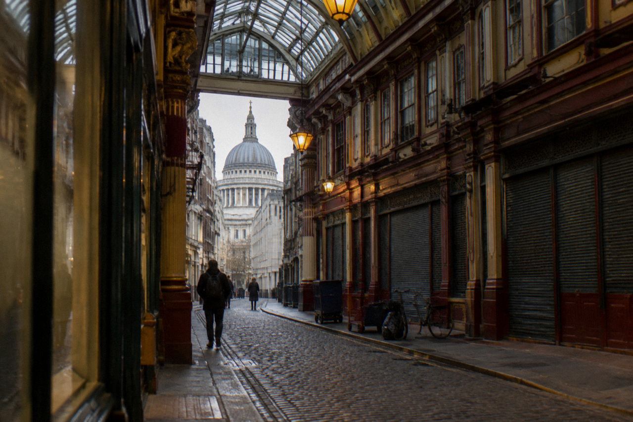Glass-roofed Victorian market arcade with painted columns and cobbled lane, cathedral dome beyond