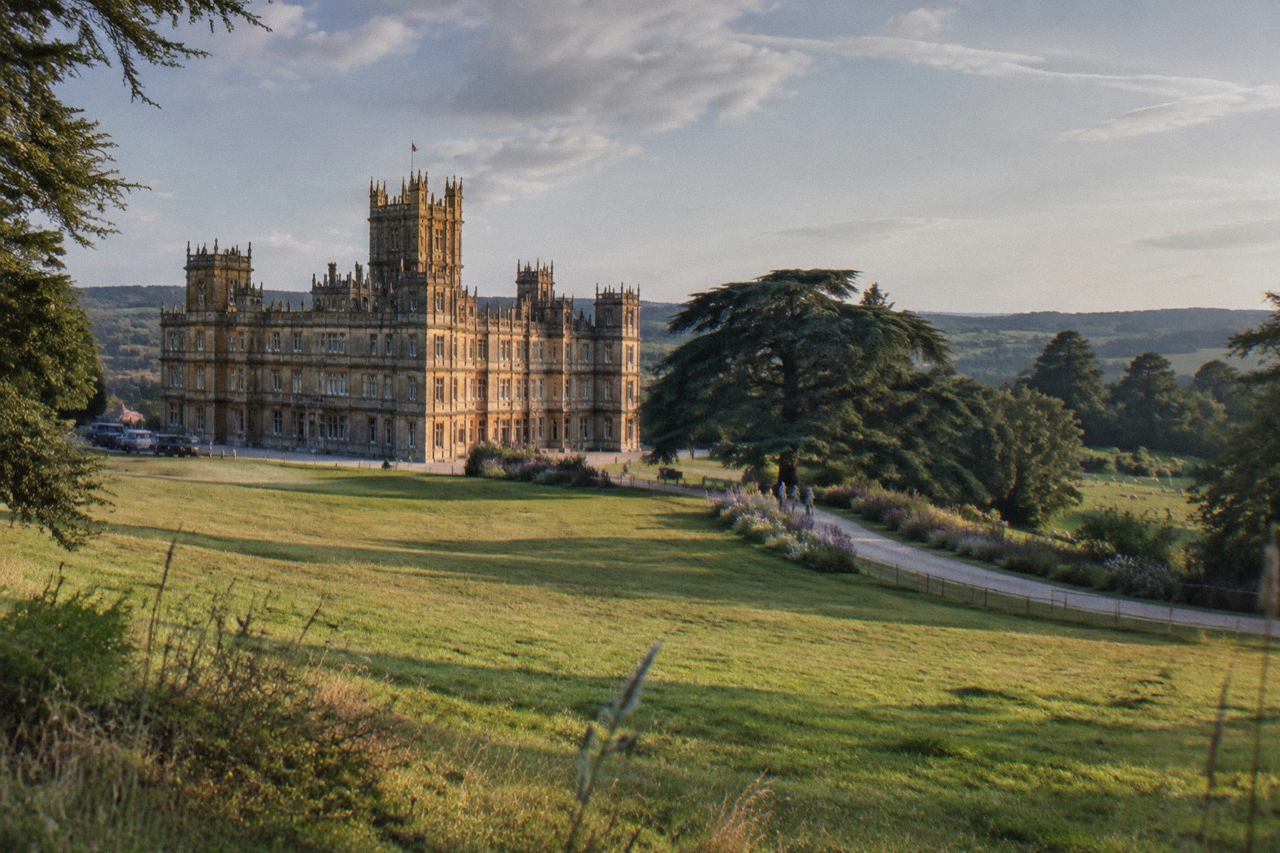 Turreted Victorian stone mansion on a lawn, parkland and sheep in warm evening light