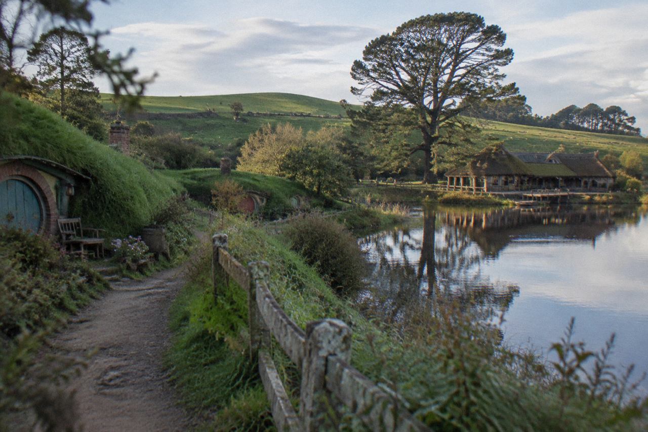 Small round-doored cottages on green hillsides beside a lake with a timber inn, morning light.
