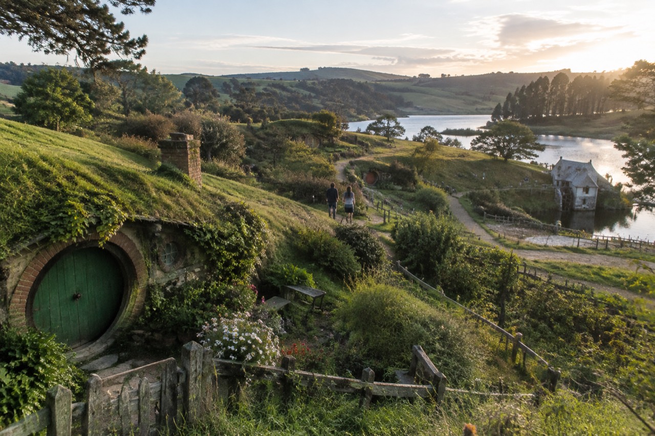 Round doors set into green hillsides with gardens, a lake and mill in golden light