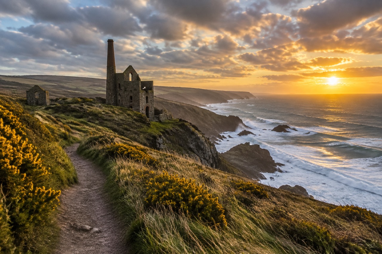 Stone mine ruins on Cornish clifftops above the sea at sunset with yellow gorse