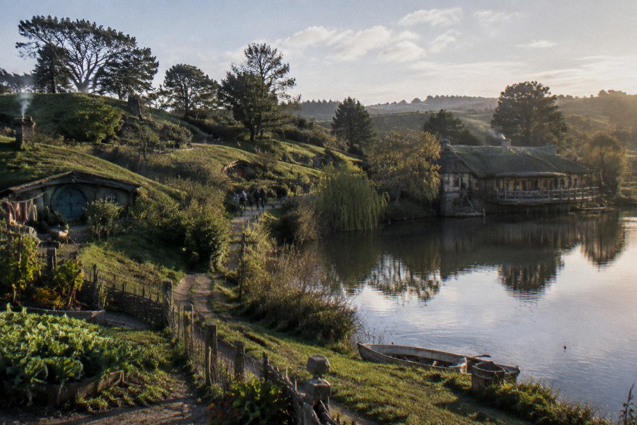 Round-doored hillside cottages and a green-roofed inn reflect in a pond at golden hour.