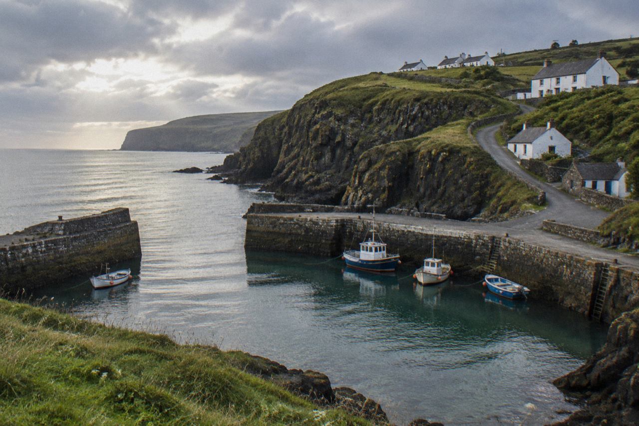 Stone fishing harbour beneath basalt cliffs on the Antrim coast, boats on calm sea