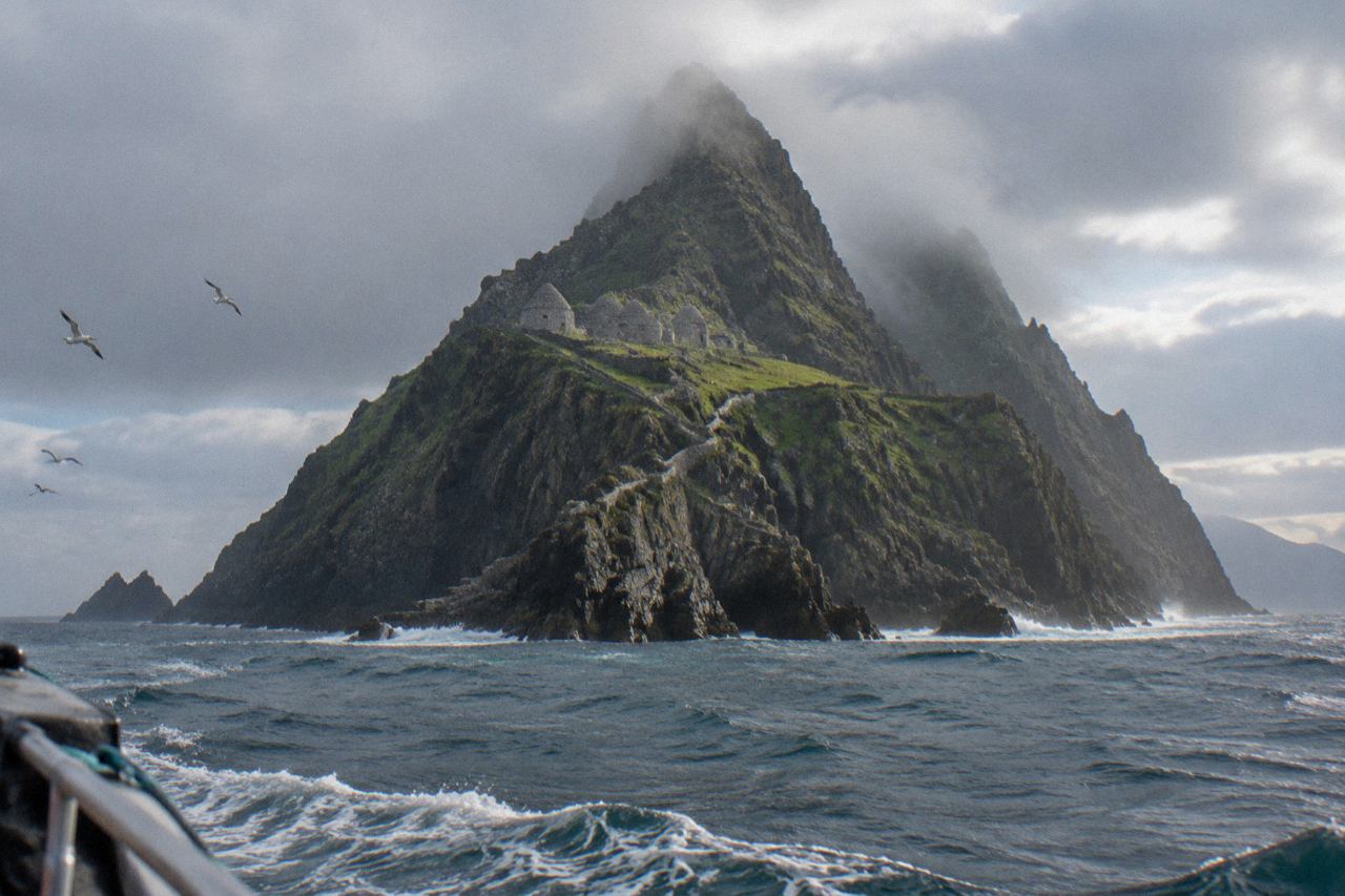 Jagged island with stone beehive huts rising from grey Atlantic sea under clouds.